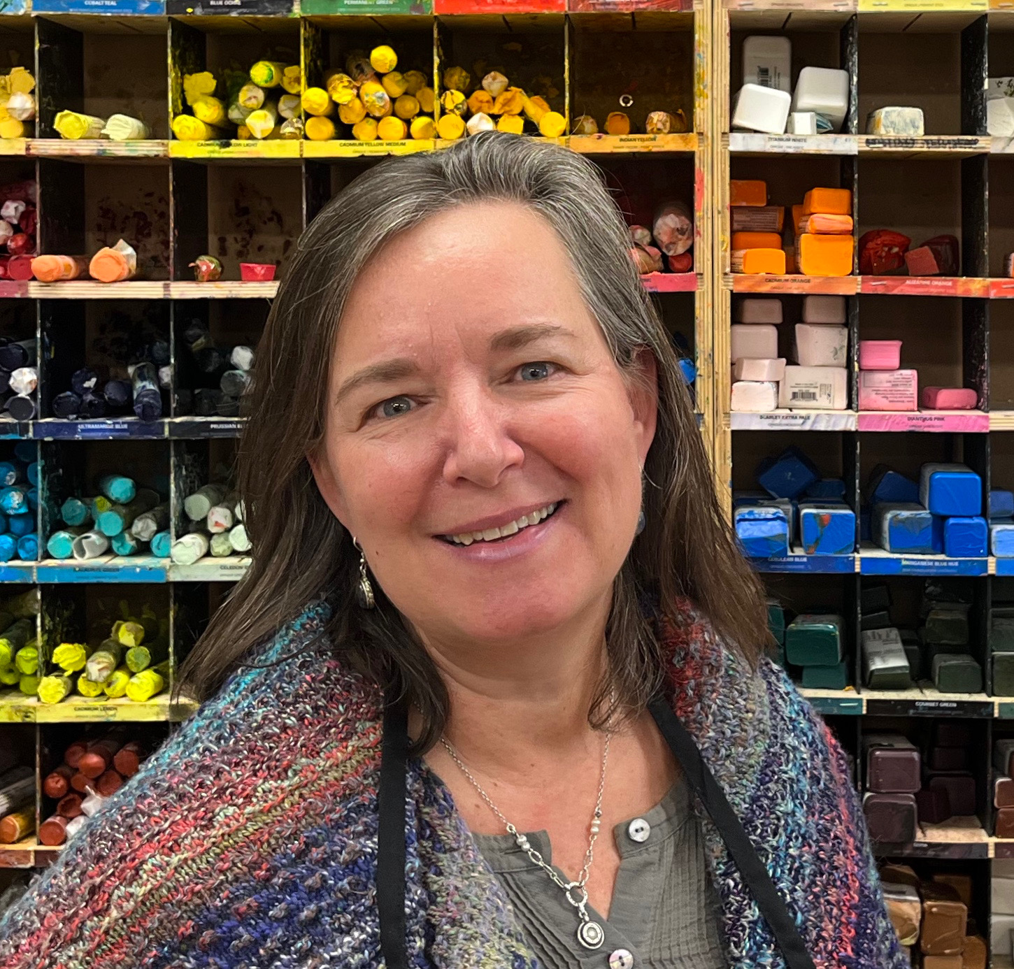 Birgitt Wolf Peterson smiling in her studio in front of shelves of pastels and pigments